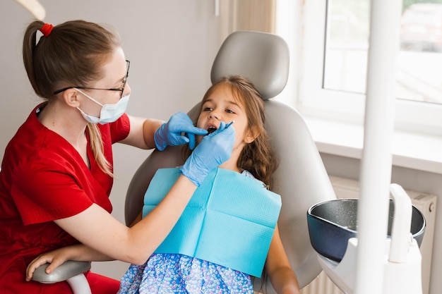 소아 치과 의사는 치통 치료를 위해 어린 소녀의 치아를 검사합니다. 어린이의 치아 통증 치과에서 소아 치과 의사와 상담