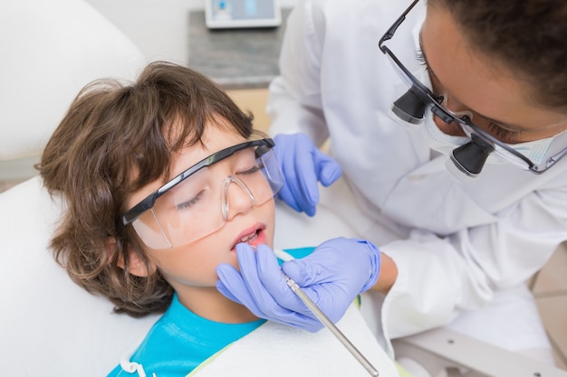 Pediatric dentist examining a little boys teeth in the dentists chair