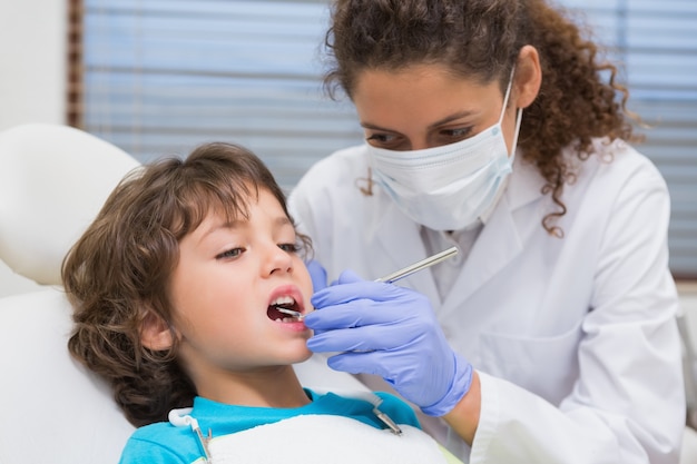 Pediatric dentist examining a little boys teeth in the dentists chair