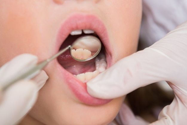 Photo pediatric dentist examining a little girls teeth in the dentists chair