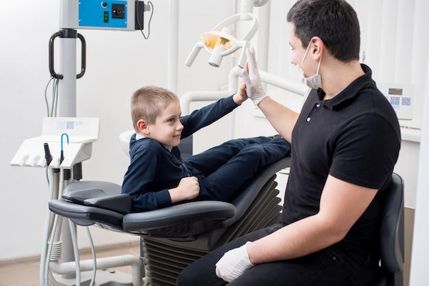 Pediatric dentist gives high five young boy, congratulate patient for a successful operation in dental office