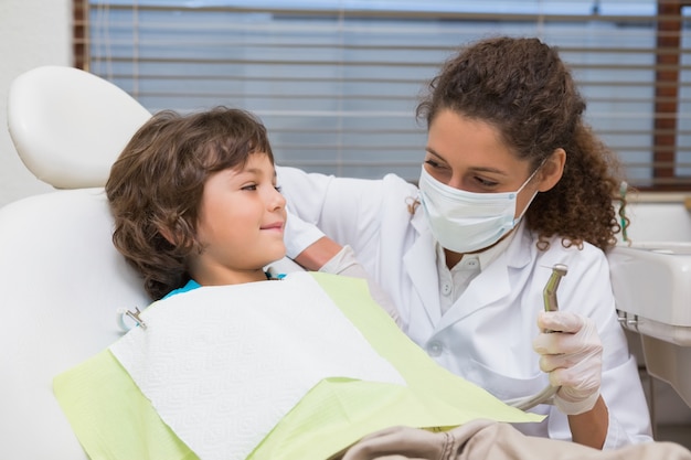 Dentista pediatrico che mostra il ragazzino nella sedia il trapano