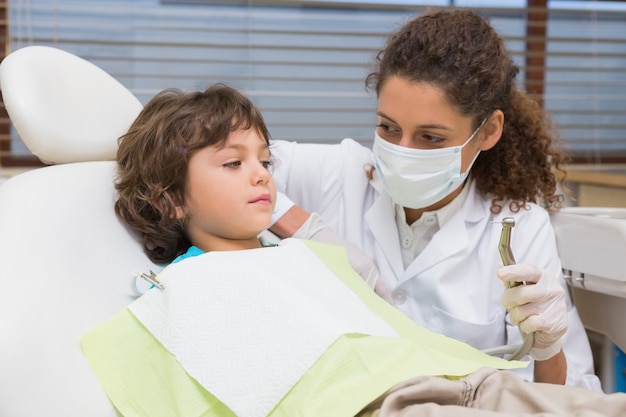 Pediatric dentist showing little boy in chair the drill