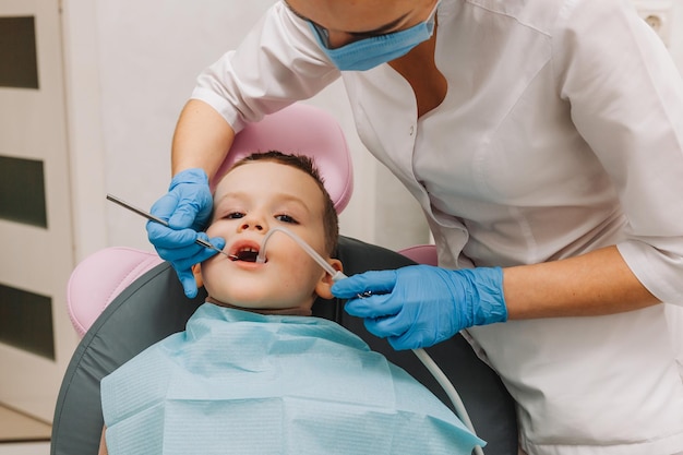 Pediatric dentist treats child caries and oral cavity of boy sitting in dentist chair during regular medical check-up