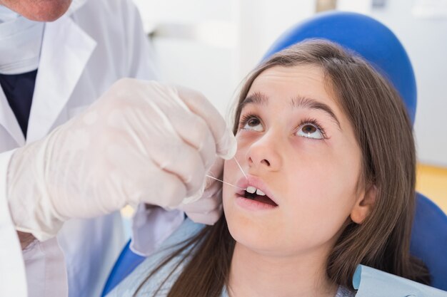 Pediatric dentist using dental floss to his young patient 