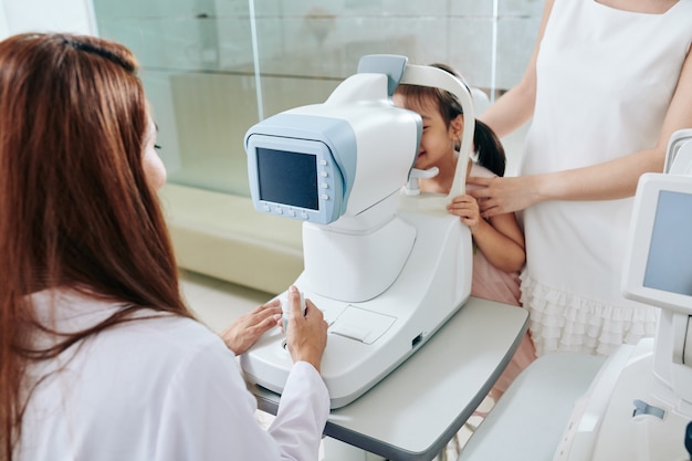 Pediatric ophthalmologist using refractometer eye test machine when checking eyesight of little girl