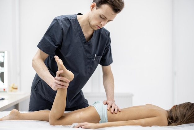 Pediatric orthopedist examines aged girl on couch in the medical office