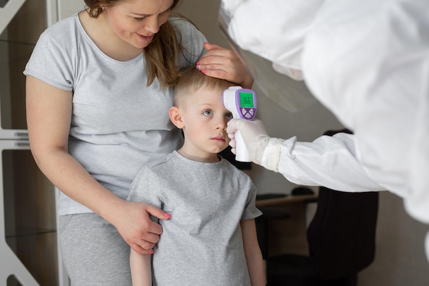 Pediatrician or doctor checks elementary age boy's body temperature using infrared forehead
