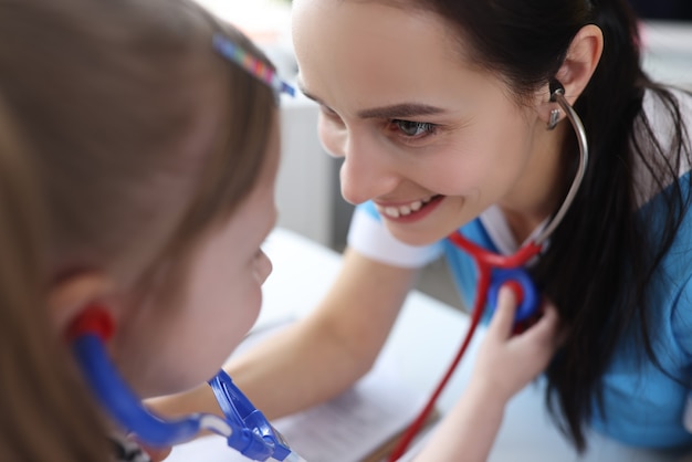 Pediatrician doctor listening to heart of little girl with stethoscope in clinic