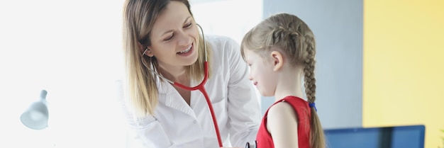 Pediatrician doctor listens with stethoscope to breathing of little girl in medical office