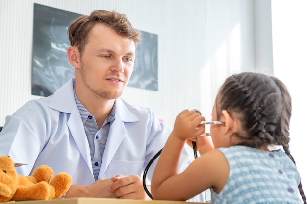 Pediatrician (doctor) man examining little girl patient using a stethoscope in hospital.