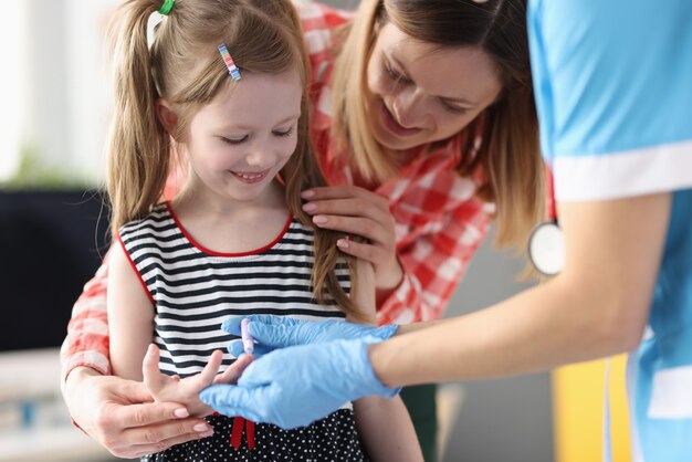 Photo pediatrician doctor takes blood test from little girl closeup