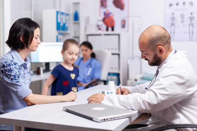 Pediatrician doctor writing symptoms disease after consultation of sick child in hospital office. Specialist in pediatry medicine talking about diagnostic and healtcare treatment