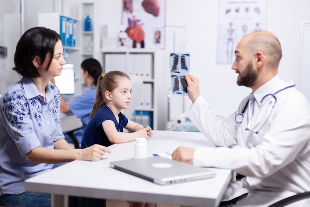 Педиатр исследует рентгенографию больного ребенка во время медицинской консультации. Врач-терапевт, специалист в области медицины, предоставляющий медицинские услуги, лечебное обследование.
