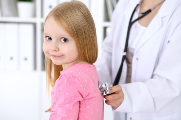 Photo pediatrician is taking care of baby in hospital little girl is being examine by doctor by stethoscope health care insurance and help concept