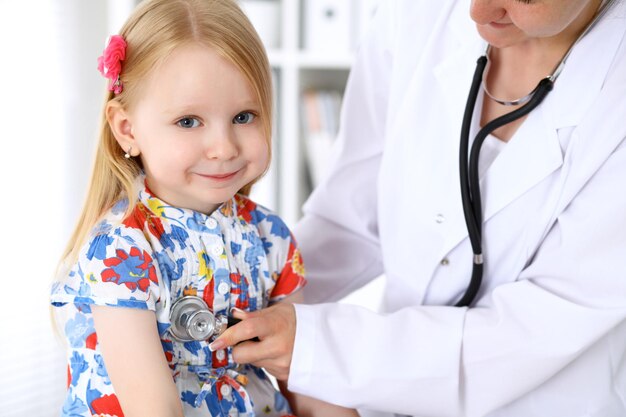 Photo pediatrician is taking care of baby in hospital little girl is being examine by doctor by stethoscope health care insurance and help concept