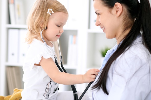 pediatrician is taking care of baby in hospital little girl is being examine by doctor with stethoscope health care insurance and help concept