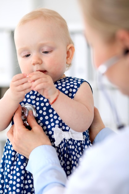 小児科医は病院で赤ちゃんの世話をしています小さな女の子は聴診器の健康保険とヘルプの概念を持つ医師によって検査されています