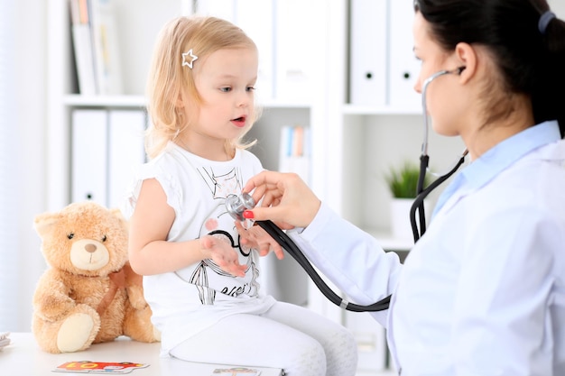 Pediatrician is taking care of baby in hospital. little girl is
being examine by doctor with stethoscope. health care, insurance
and help concept.