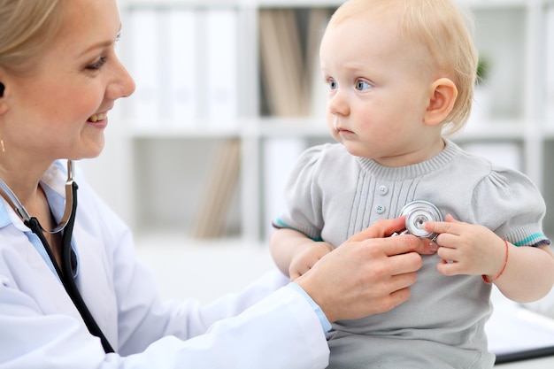 Pediatrician is taking care of baby in hospital. Little girl is being examine by doctor with stethoscope. Health care, insurance and help concept.