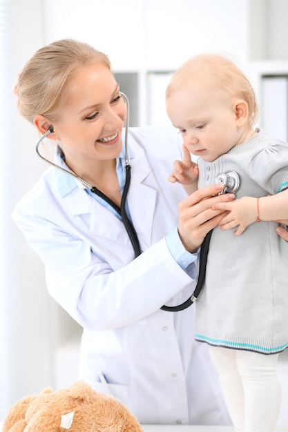 Pediatrician is taking care of baby in hospital. Little girl is being examine by doctor with stethoscope. Health care, insurance and help concept.