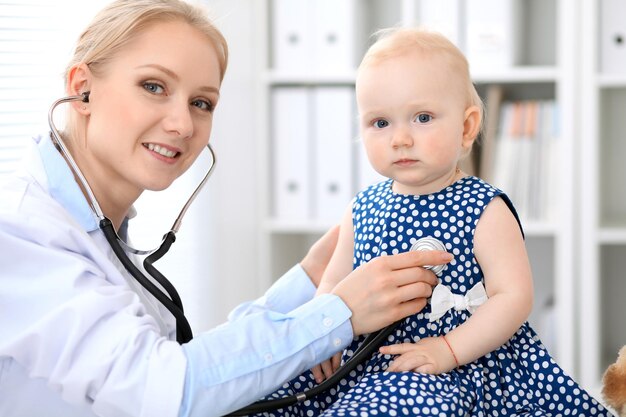 Pediatrician is taking care of baby in hospital. Little girl is being examine by doctor with stethoscope. Health care, insurance and help concept.