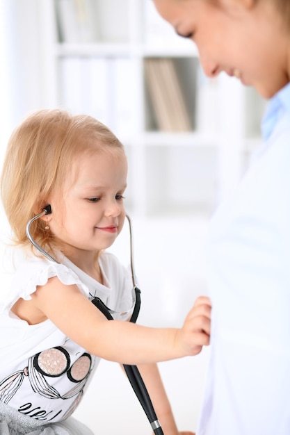 Pediatrician is taking care of baby in hospital. Little girl is being examine by doctor with stethoscope. Health care, insurance and help concept.