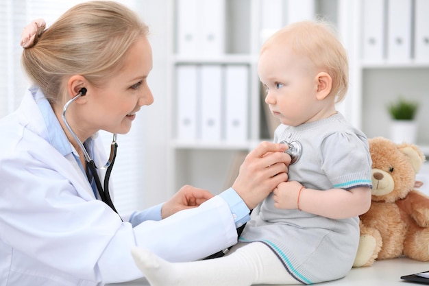 Pediatrician is taking care of baby in hospital. Little girl is being examine by doctor with stethoscope. Health care, insurance and help concept.