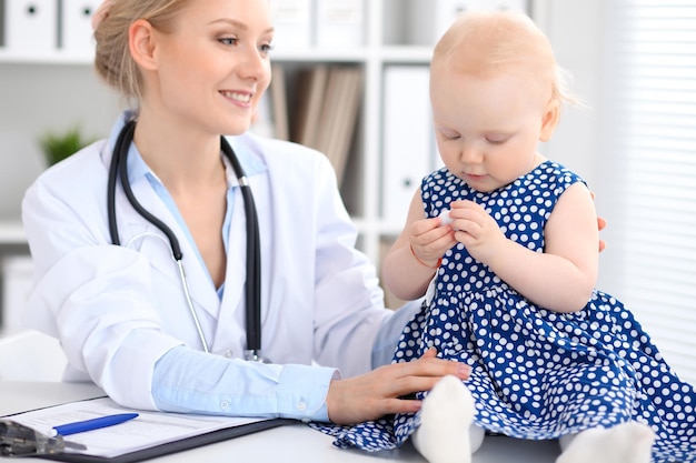 Pediatrician is taking care of baby in hospital. Little girl is being examine by doctor with stethoscope. Health care, insurance and help concept.