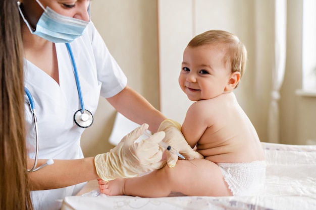 pediatrician or nurse giving an intramuscular injection of a vaccine to leg of little baby boy