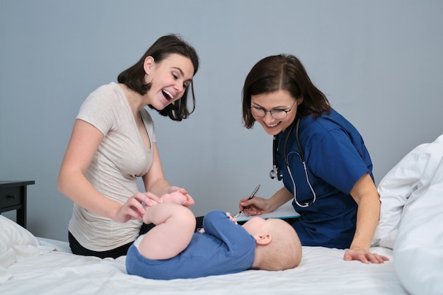 Pediatrician woman doctor in blue uniform with stethoscope talking to young mother of little boy