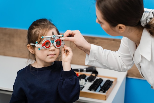 Pediatrische oogarts draagt een bril met proefmontuur op kind Onderzoek met oogarts voor selectie van proefbrilmontuur om het visuele oogsysteem te onderzoeken