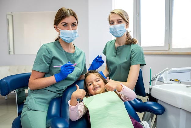 Pediatrische vrouwelijke tandarts met assistent met kindmeisje patiënt duimen opdagen