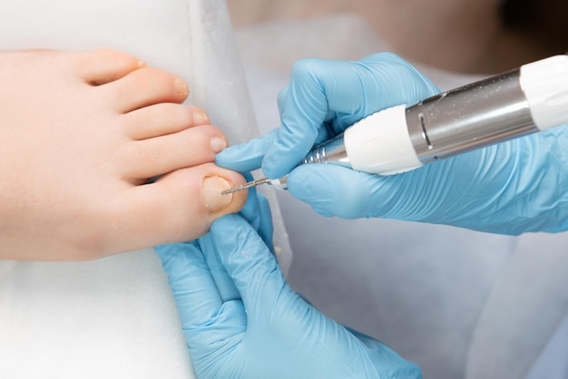 Photo pedicure expert utilizes an electric drill machine to perform a professional hardware pedicure on