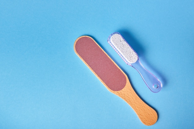 Pedicure grater with wooden handle and pumice stone with plastic handle brush on blue background