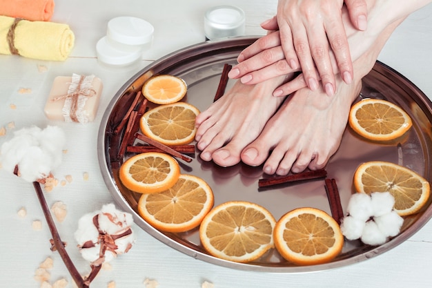 Pedicure and manicure in the spa salon with sliced oranges,\
cinnamon and cotton on a white wooden table