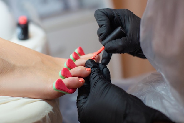 Pedicure master applying red gel polish on nails in beauty salon