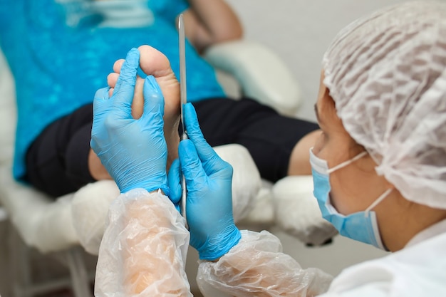 The pedicure master cleans the heel of the foot from dry skin with a tool.