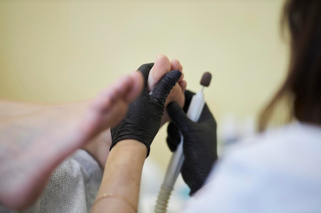 Pedicure master removes dry skin from the client's heel with a grinding tool closeup