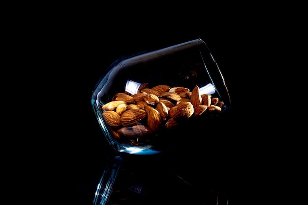 Peeled almond in jar wineglass bucket on a black isolated background Row of bowls with almond nuts front view