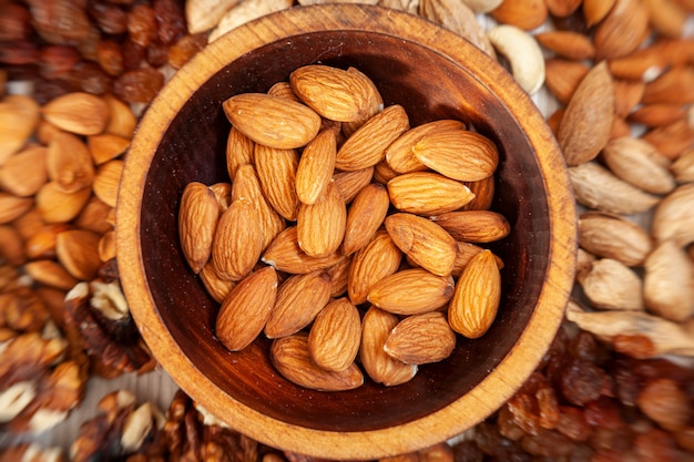 Peeled almonds in a wooden cedar plate on the background a scattering of various nuts.