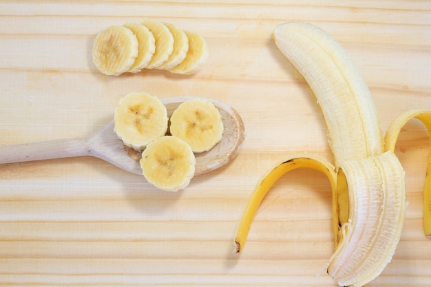 Photo peeled banana on wood next to slices on wooden spoon, top view