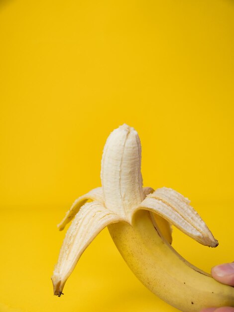 Peeled banana on yellow background with copy space