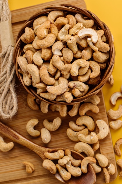 Peeled cashew nuts in a vine basket and scattered on a yellow background
