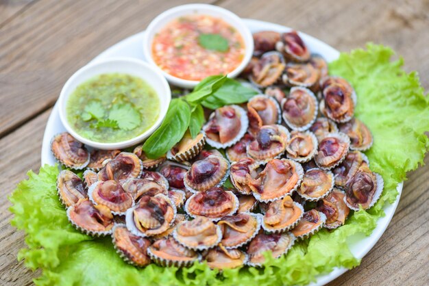 Peeled cockles with seafood sauce and vegetable salad lettuce on plate  wooden background, Fresh raw shellfish blood cockle ocean gourmet seafood in the restaurant, sea shells food