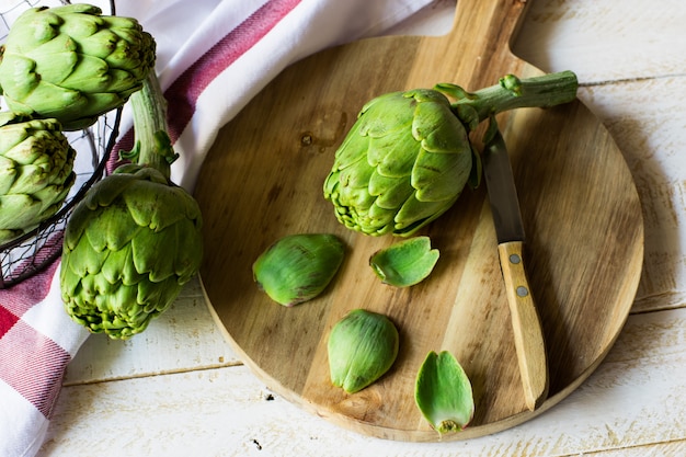 Peeled fresh artichoke preparing for cooking, wood cutting board, knife, vegetables in basket