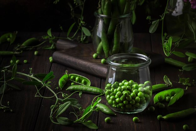 peeled fresh sweet green peas in glass jar dark wooden kitchen table background copy space selective focus