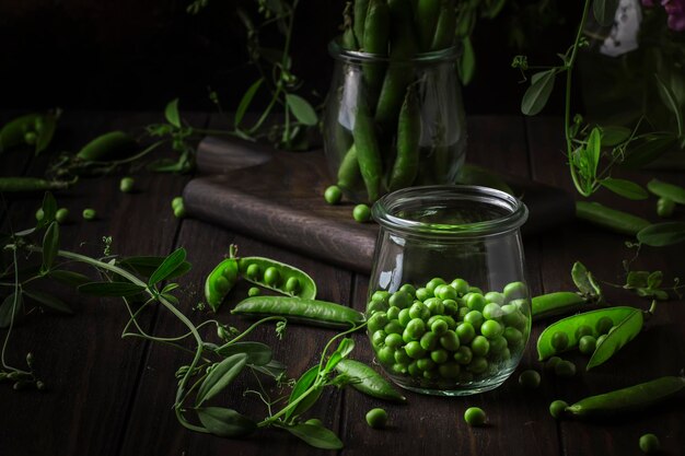 Peeled fresh sweet green peas in glass jar dark wooden kitchen table background copy space selective focus