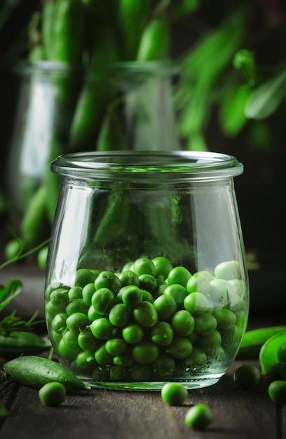 Peeled fresh sweet green peas in glass jar dark wooden kitchen table background copy space selective focus