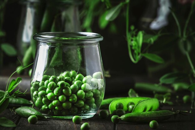 Peeled fresh sweet green peas in glass jar dark wooden kitchen table background copy space selective focus